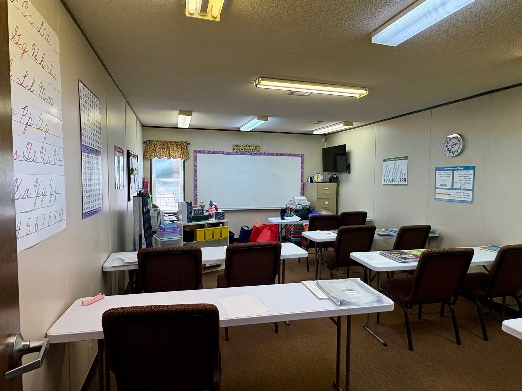 Classroom interior with tables, chairs, whiteboard, and learning materials.