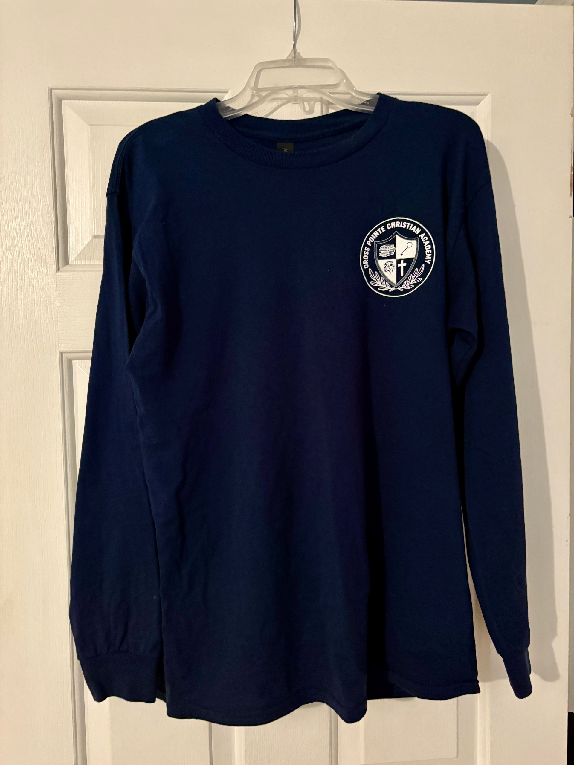 Navy blue long-sleeved shirt with a white circular logo on the upper left chest, hanging on a white door.