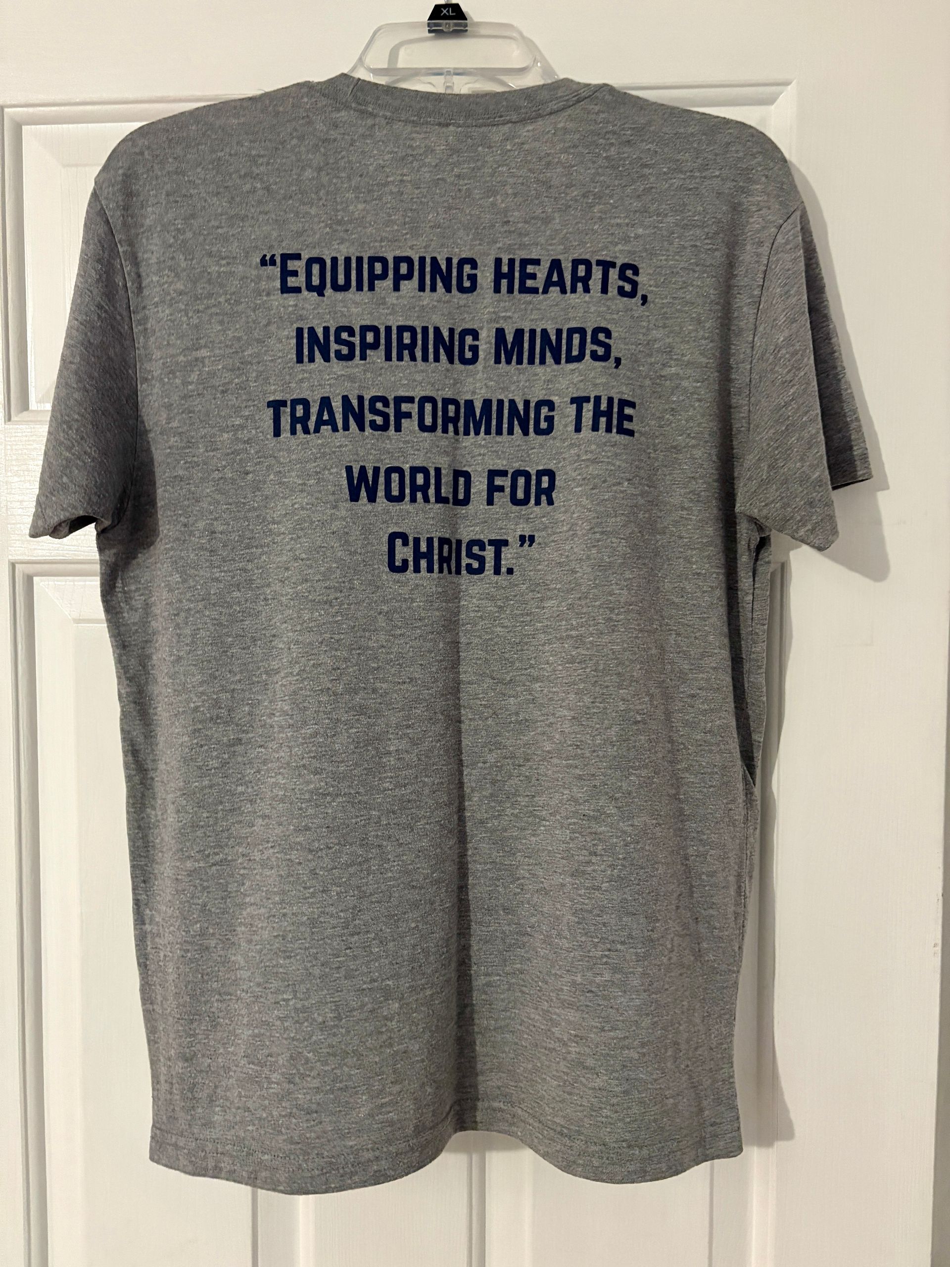 Gray t-shirt with dark blue text: “Equipping Hearts, Inspiring Minds, Transforming the World for Christ.”