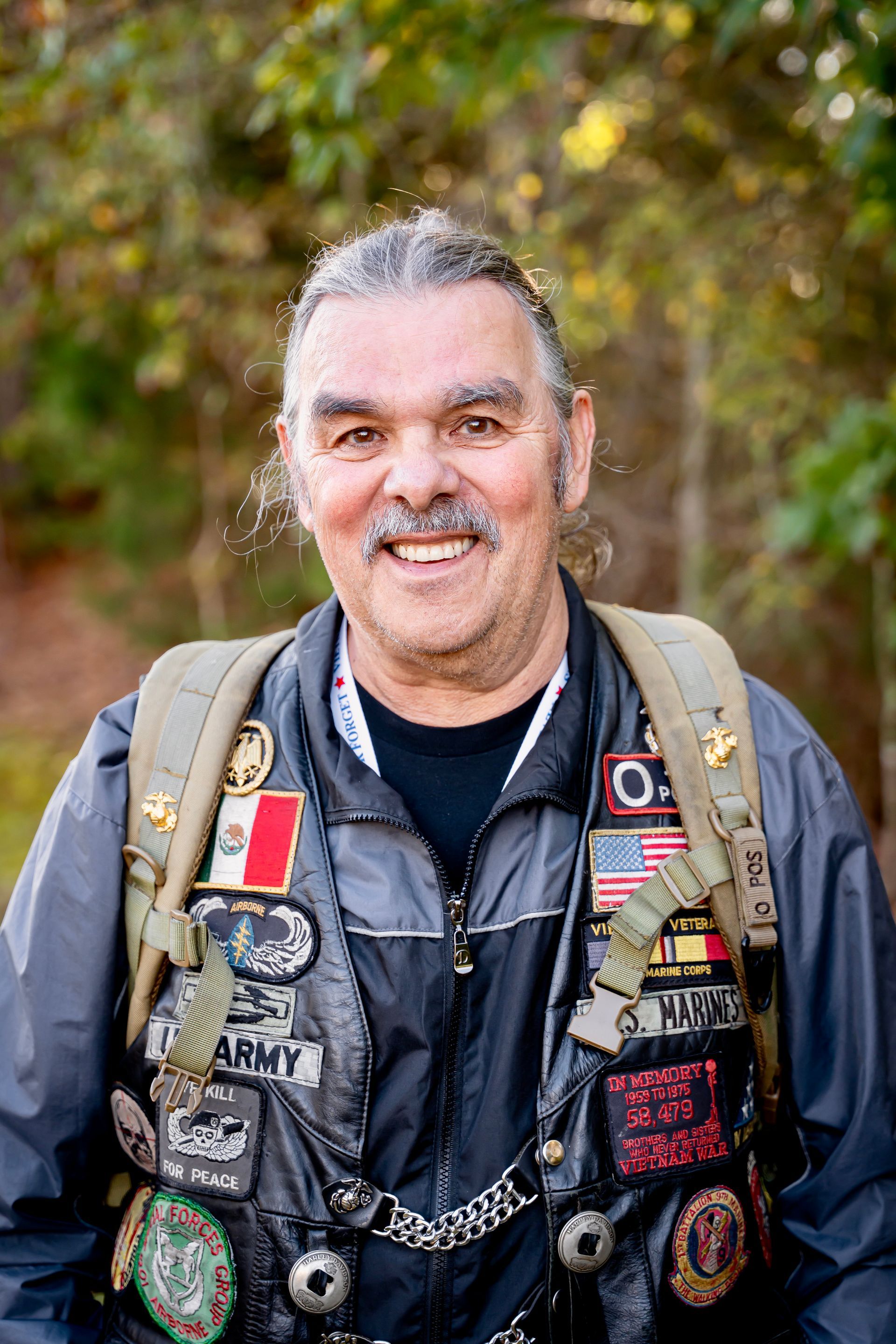 Man wearing jacket with patches, smiling outdoors.