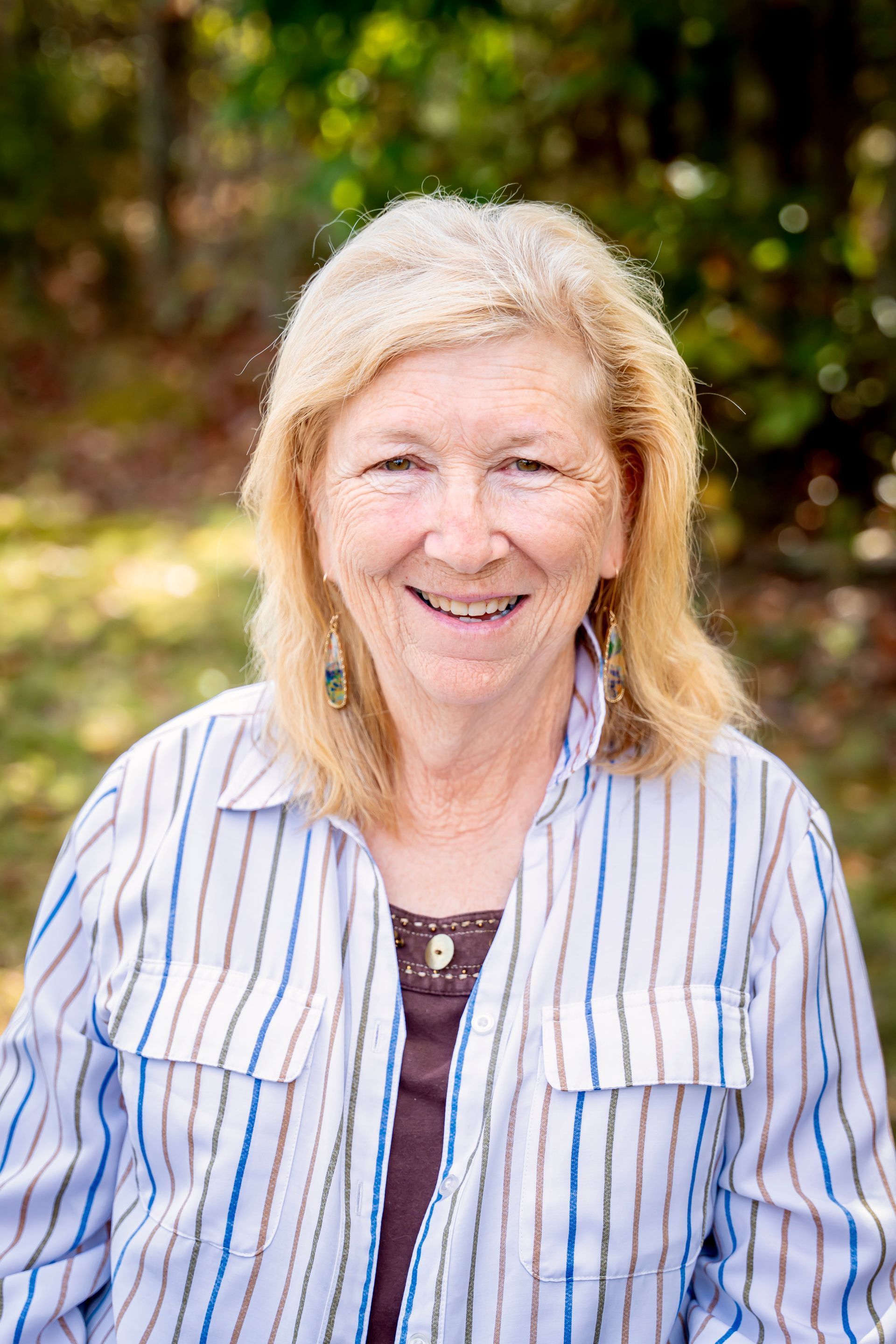 Woman with blonde hair wearing a striped shirt smiles outdoors.