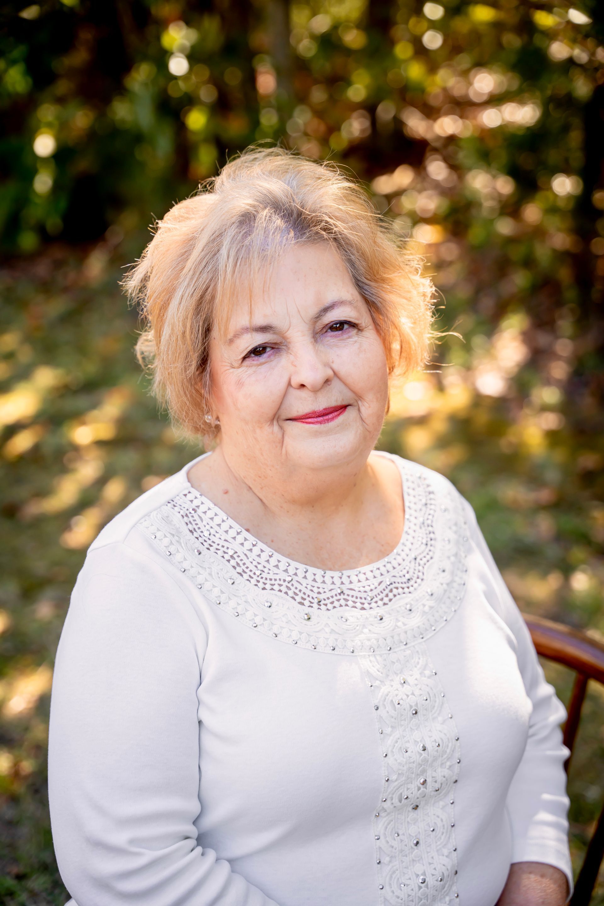 Woman in white sweater smiling outdoors with trees in the background.