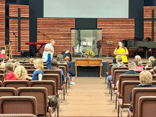 People in a church auditorium, two speakers on stage with a wooden backdrop.