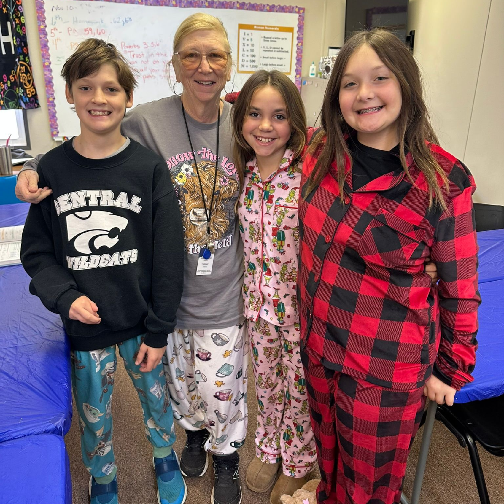 Four people in pajamas pose in a classroom. Two children and an adult smile at the camera.