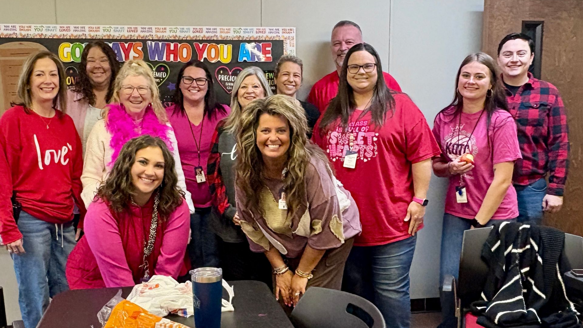 Group of people in red and pink shirts pose indoors.