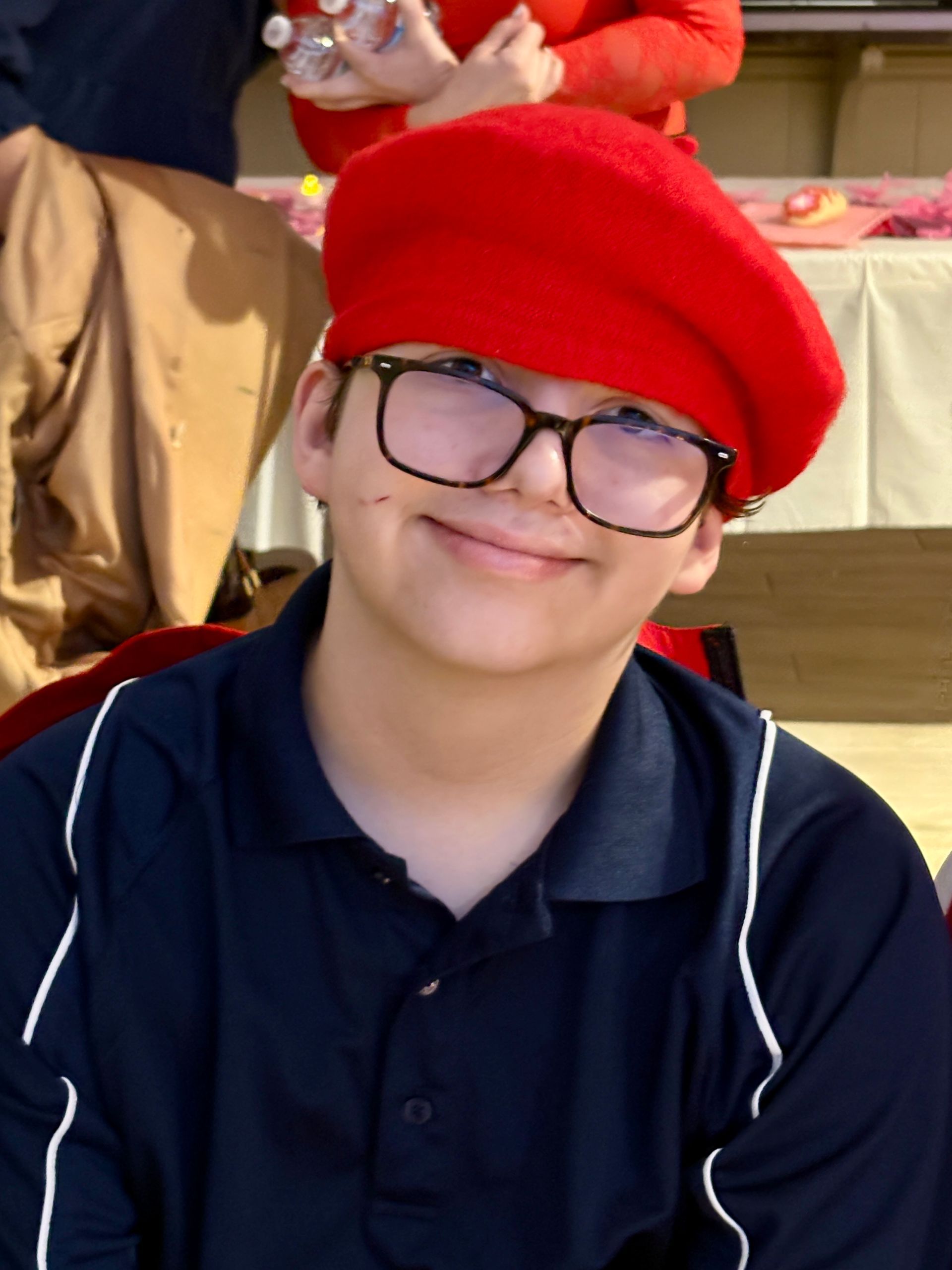 Person with glasses and a red beret smiles, wearing a dark blue polo shirt.
