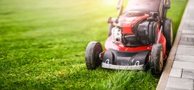 Red lawn mower trimming grass along a stone garden edge Red lawn mower trimming grass along a stone garden edge