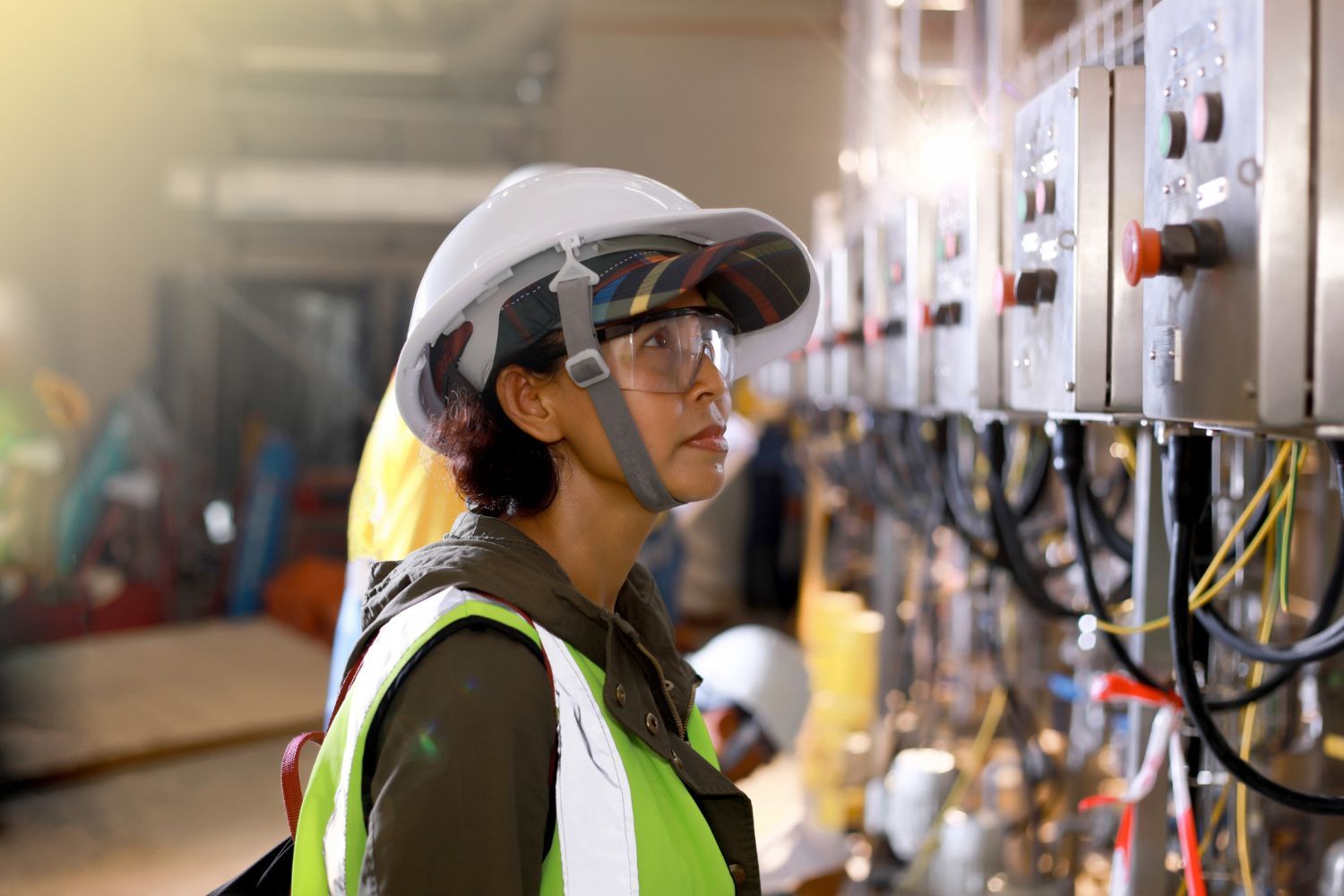 A man wearing a yellow hat is working on an electrical panel.