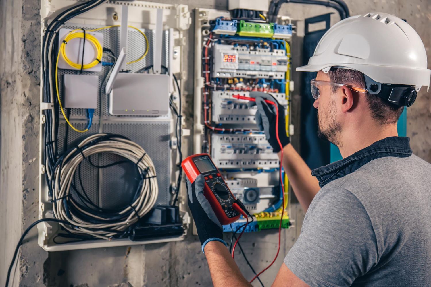 An electrician is working on an electrical box with a multimeter.