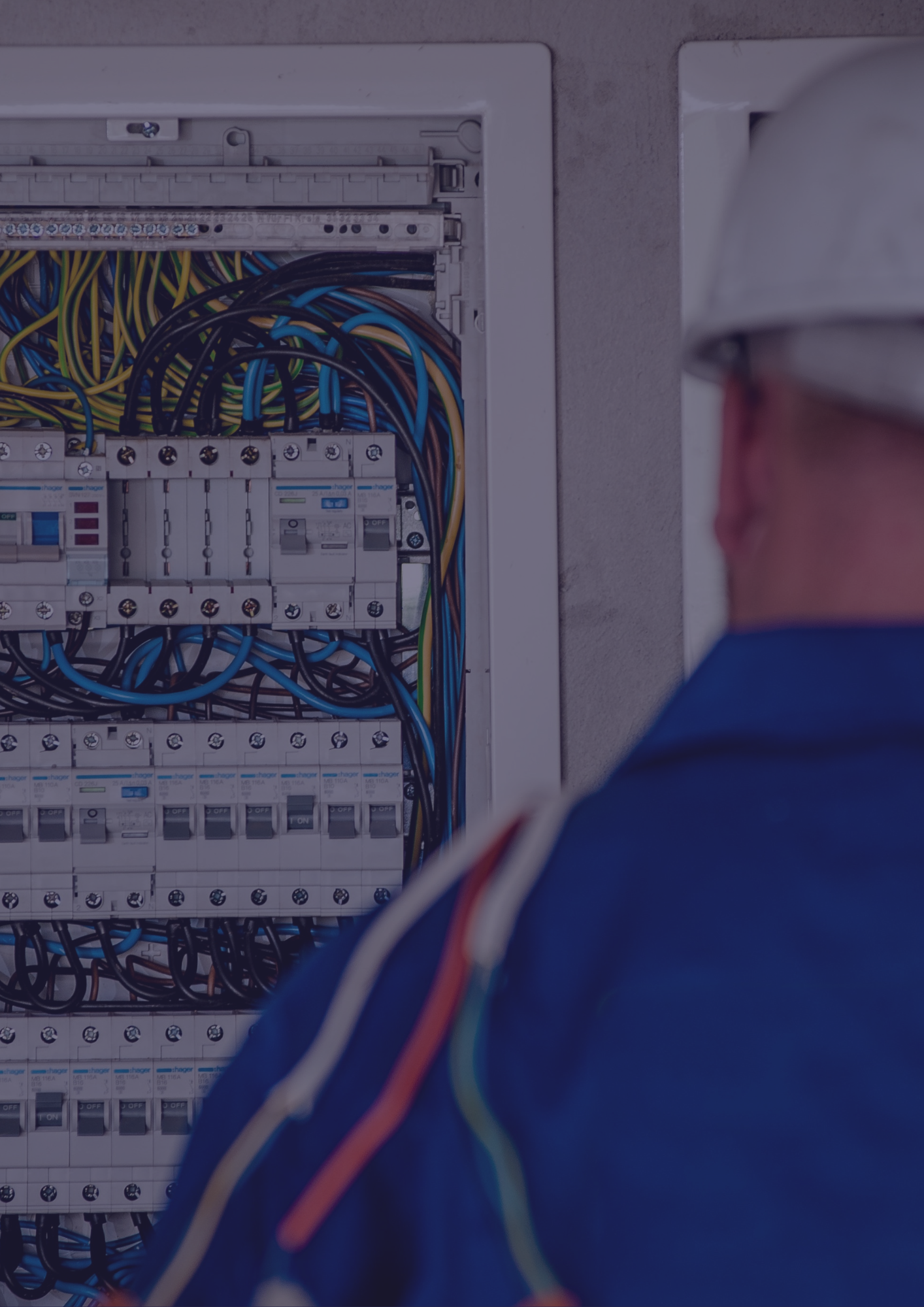 A man wearing a hard hat is working on an electrical box.