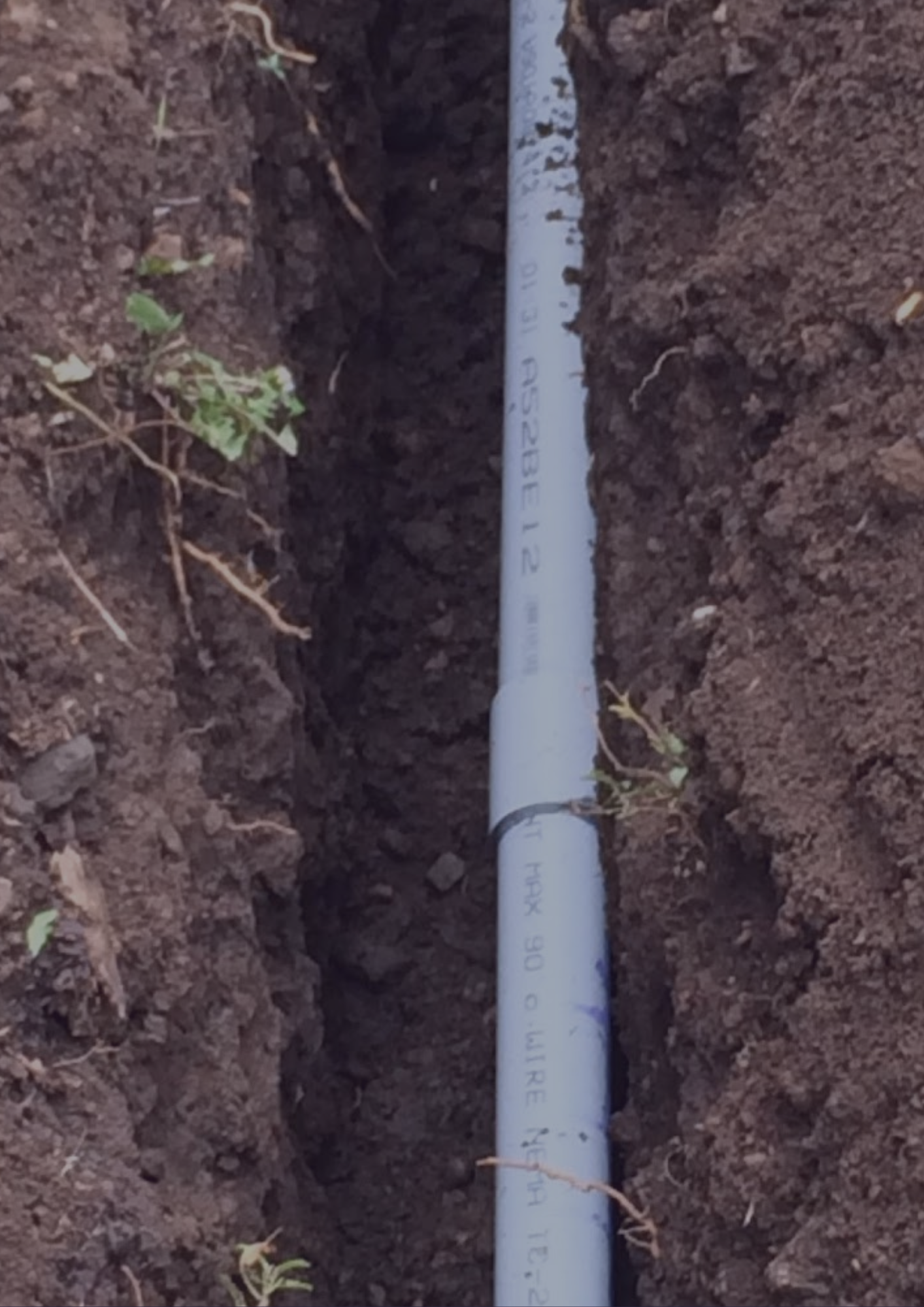 A blue pipe is laying in the dirt and has the word pvc on it