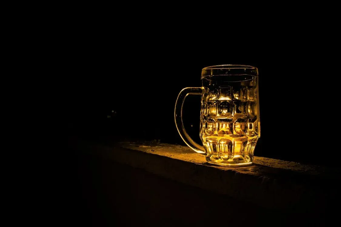 A glass of beer is sitting on a table in the dark.