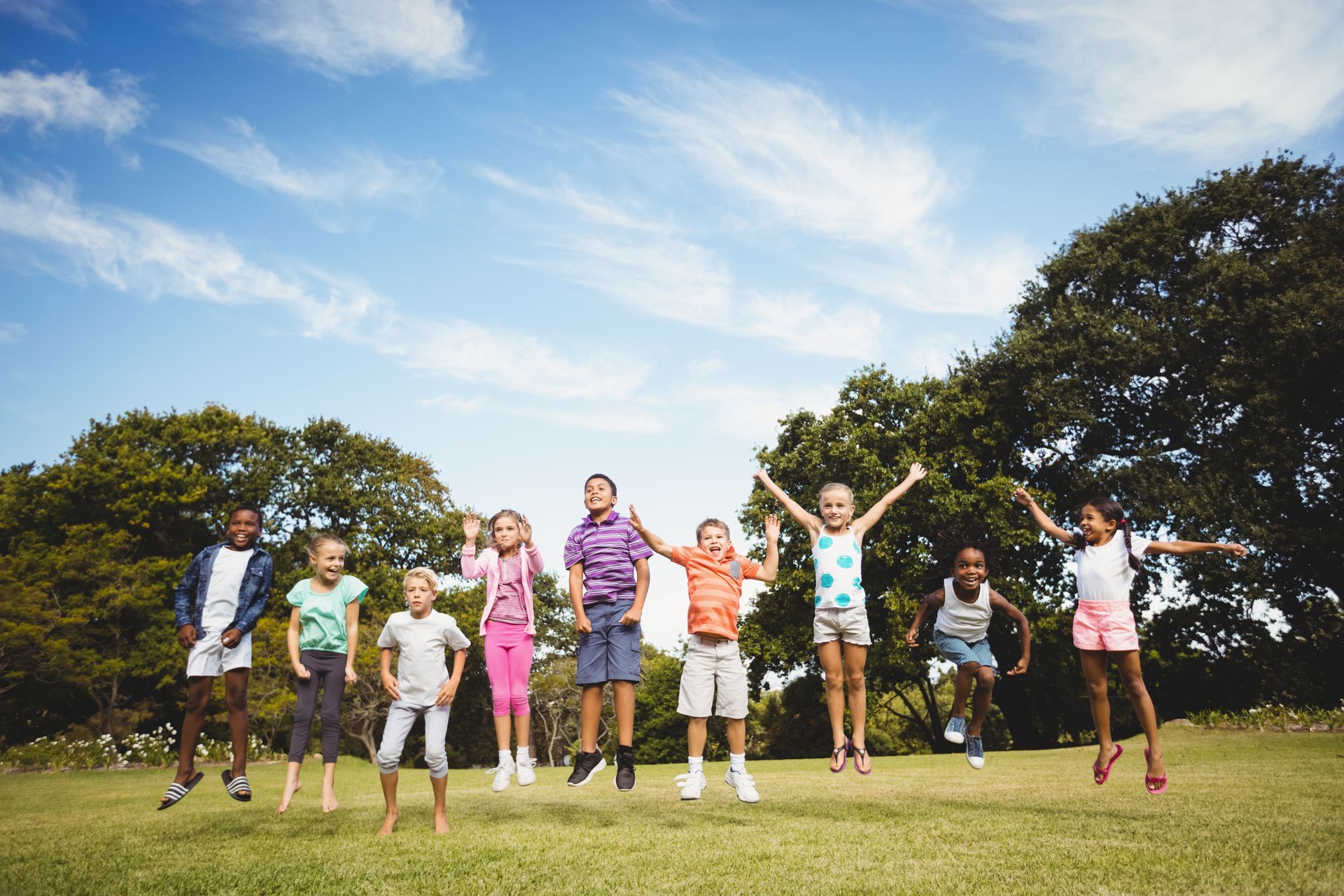 Children jumping in a grassy field under a sunny sky.