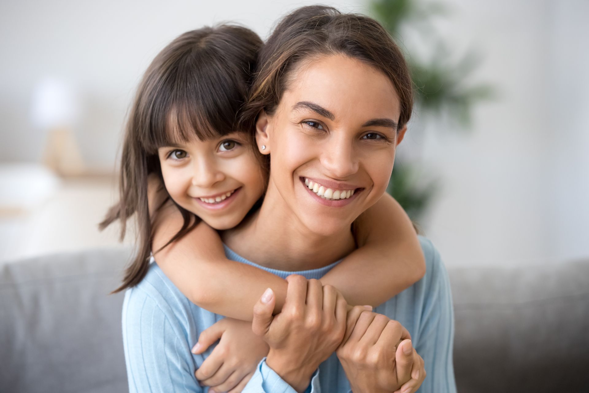 Woman and child smiling, embracing each other. Child has arms around the woman's neck.