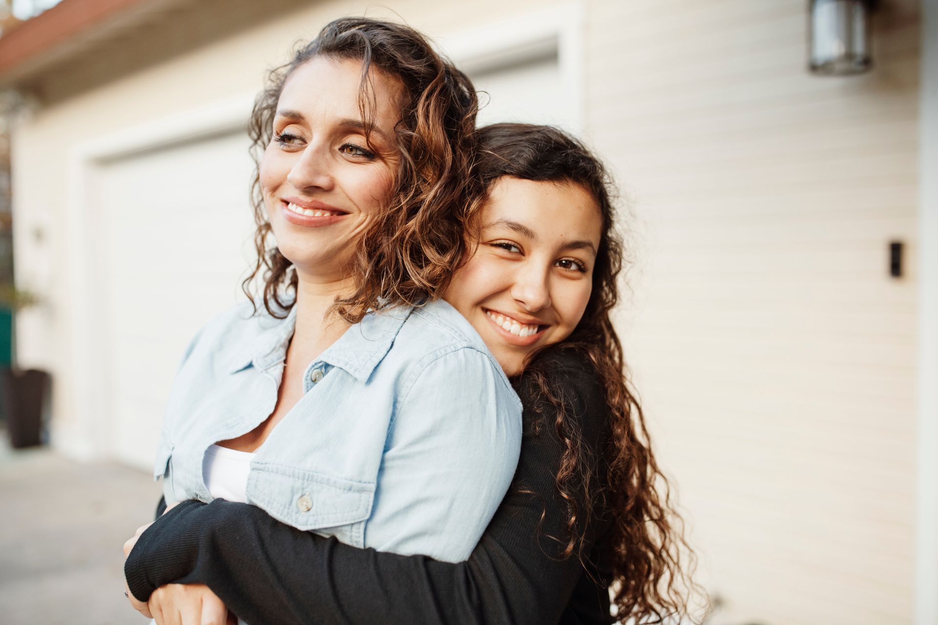 Woman smiles as a younger person hugs her from behind, both looking toward the sunlight.