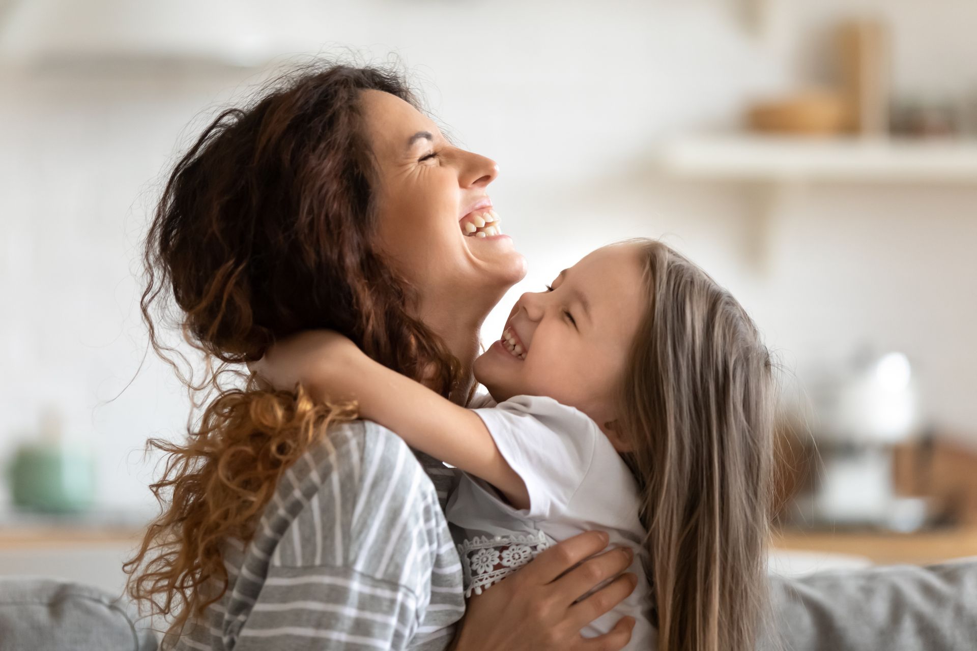 Woman and child embracing and laughing. Indoors, blurred background.