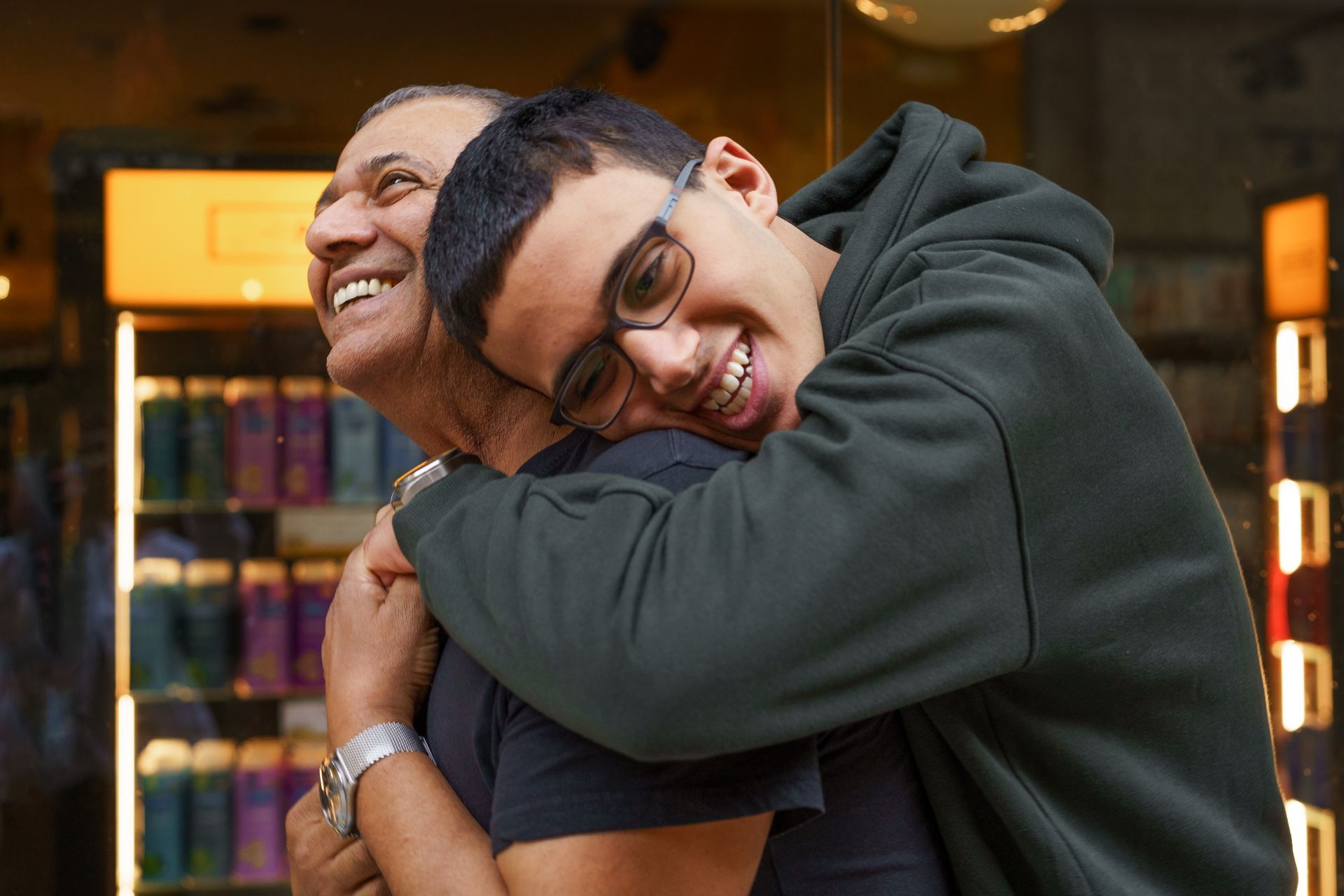 Man embraces another, both smiling; background of a store.