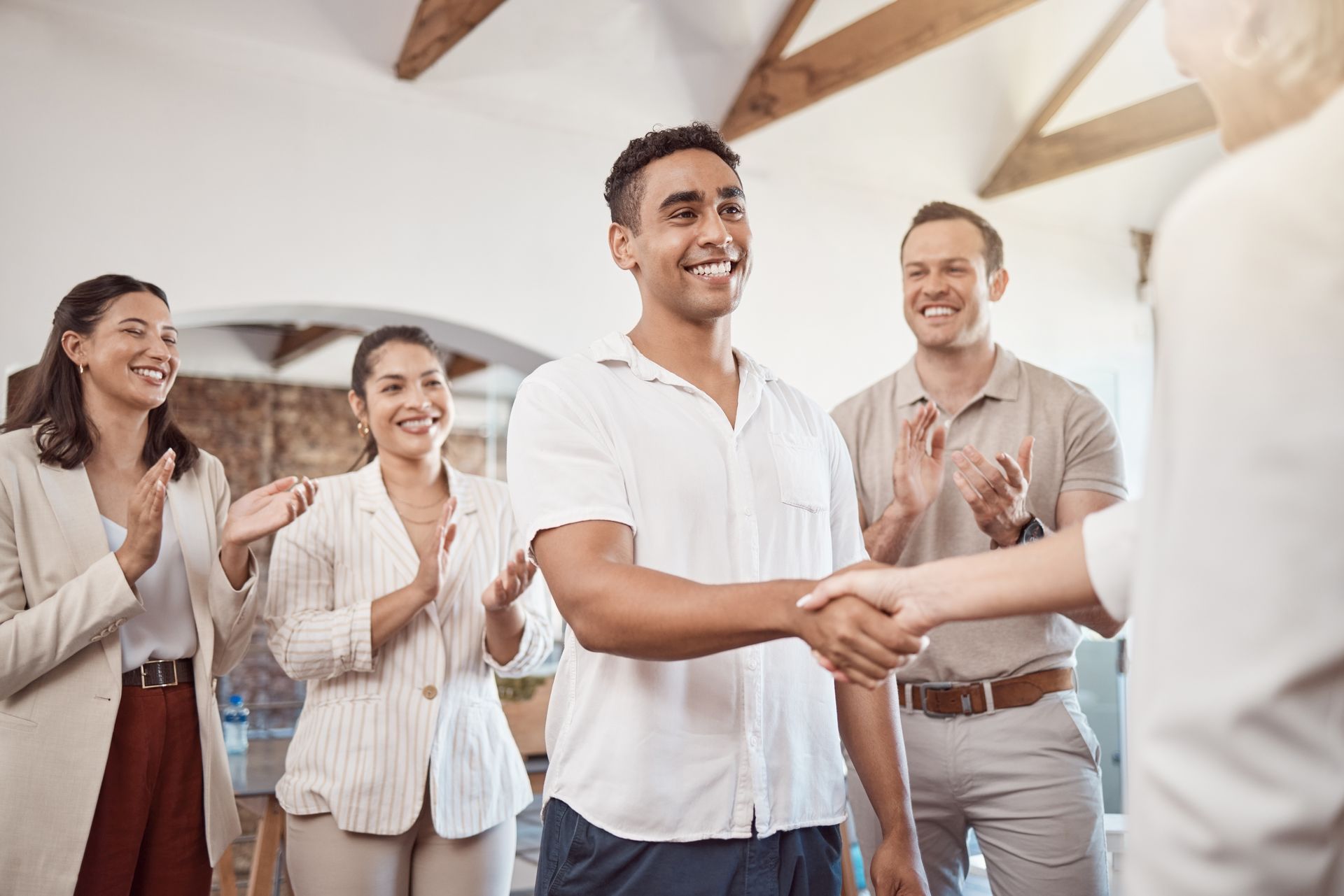 Man shaking hands, smiling, surrounded by coworkers clapping in an office.