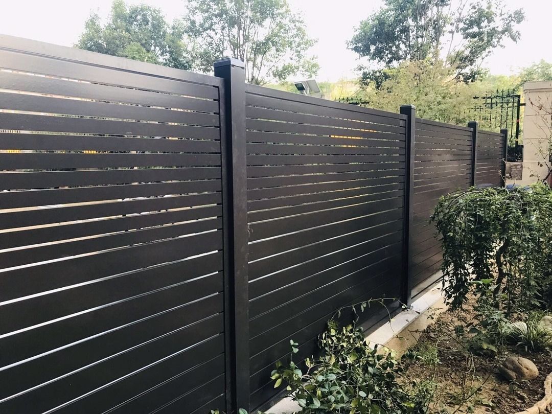 White metal fence with open gate against a backdrop of trees and a blue sky.
