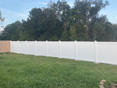 White vinyl fence in a backyard with green grass and trees.