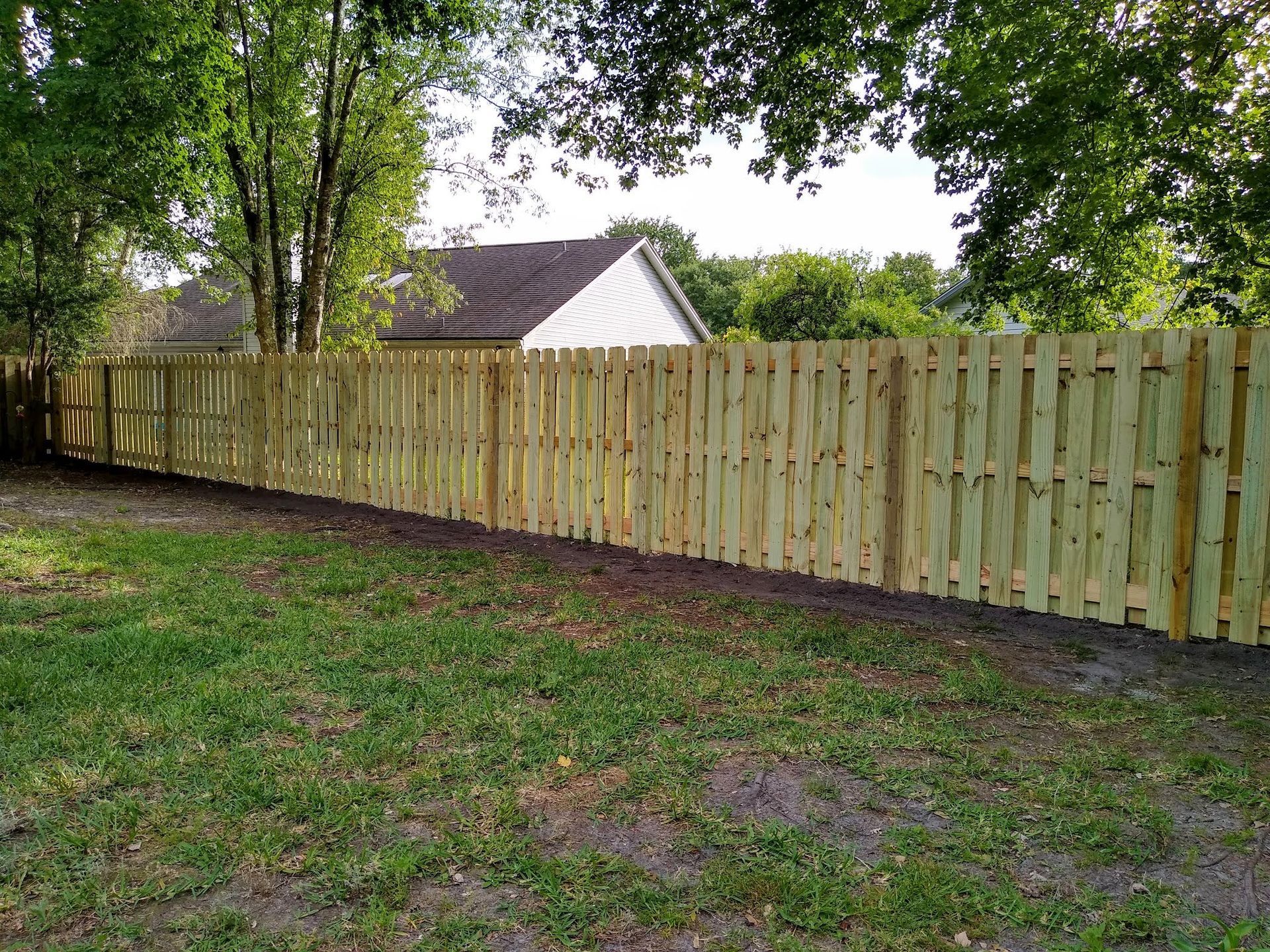 White picket fence encloses a green lawn in front of a house with a gray roof.