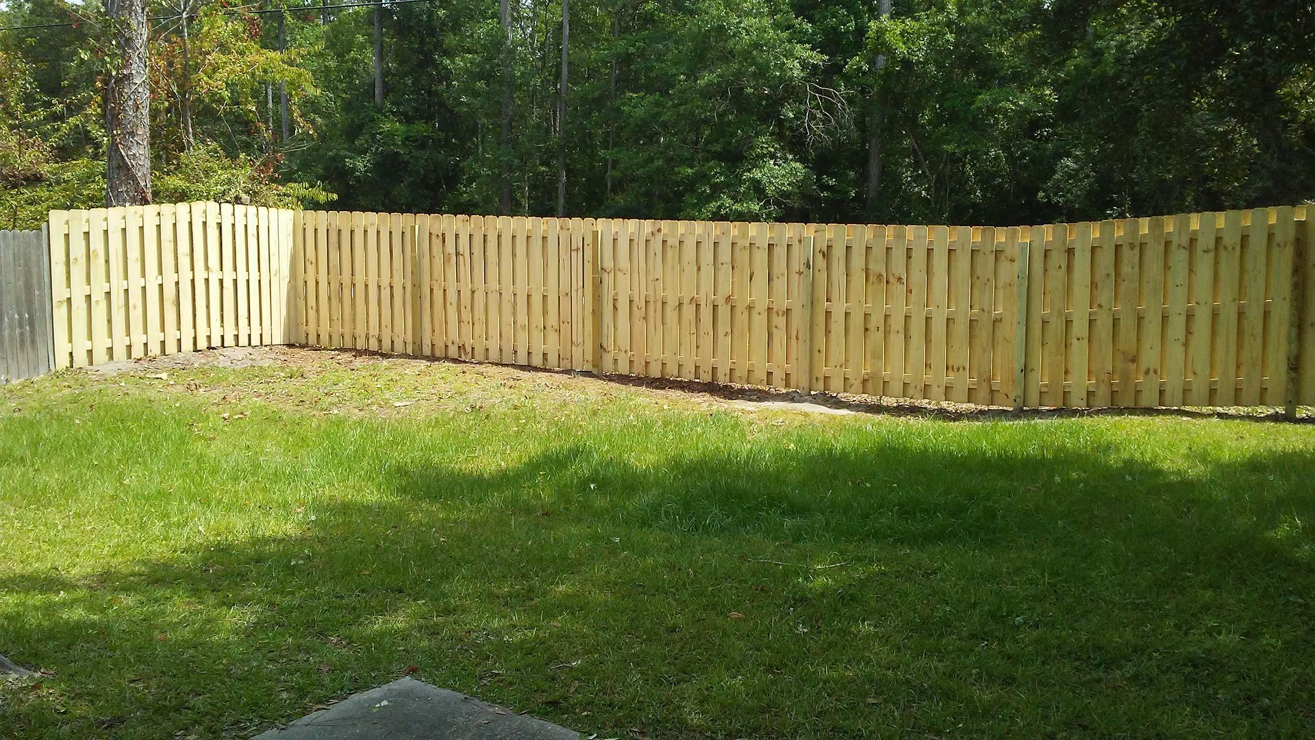 Person measuring a wooden fence with a yellow tape measure on a sunny day.