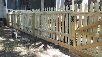 Wooden picket fence with gate; cat sits in the grass beside it.