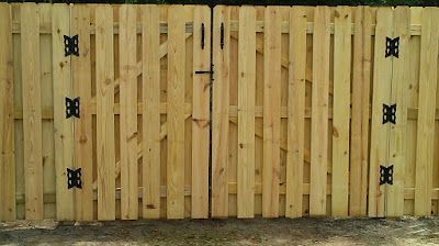 Wooden fence with double gate, black hardware, and vertical boards.