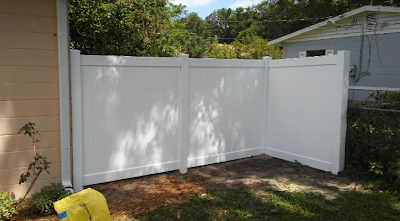 White vinyl fence in a yard, attached to the side of a beige house.