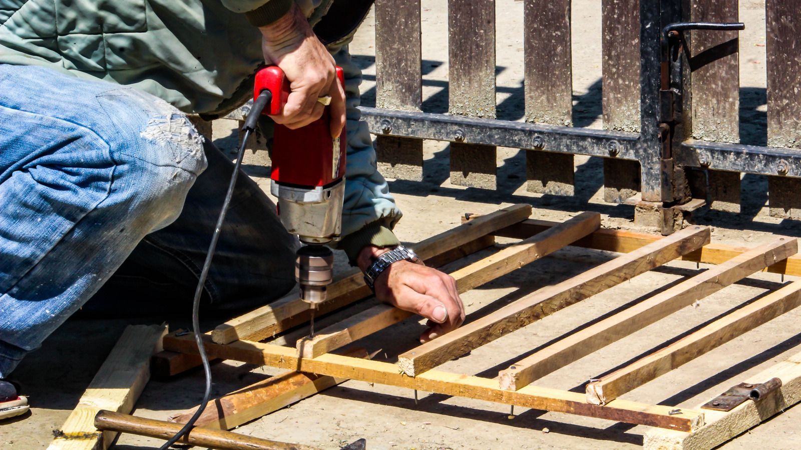 Person using a red drill to assemble wooden slats outdoors.