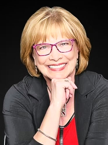 Smiling person with pink glasses resting chin on hand against a black background