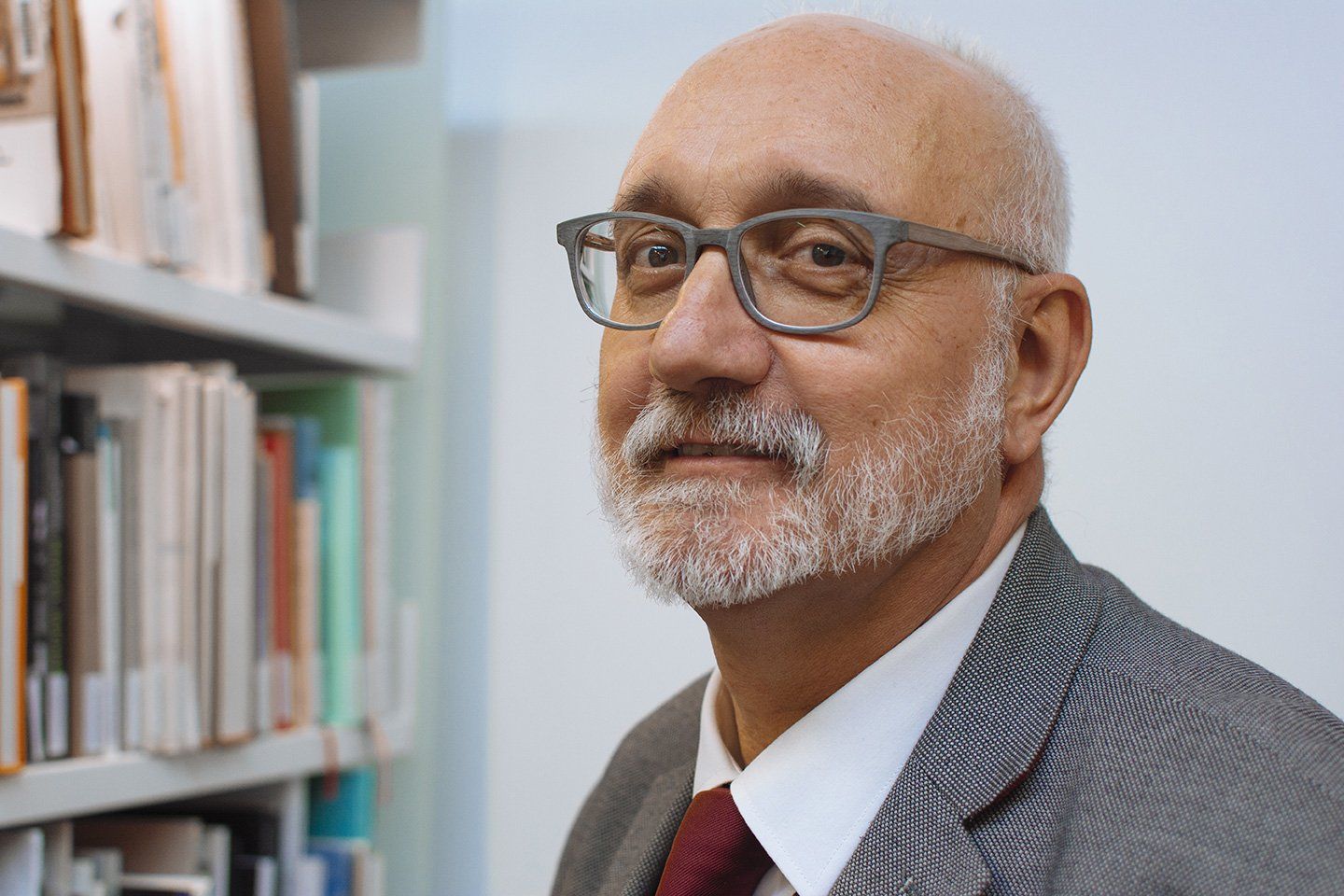 A man with a beard and glasses is standing in front of a bookshelf.