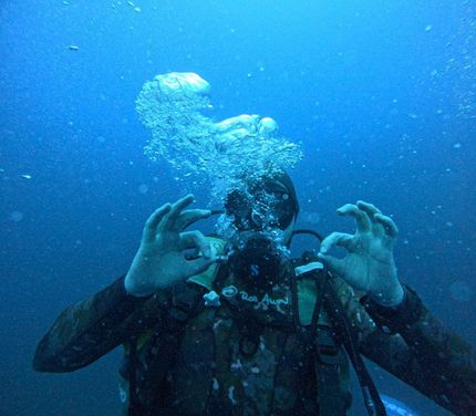 Scuba diver underwater, making an OK sign amid rising bubbles in blue water