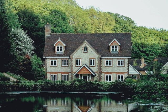 A large house is sitting next to a lake in the middle of a forest.