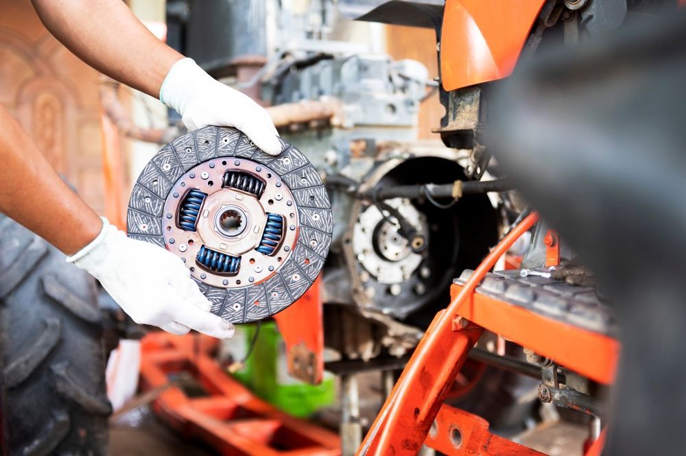 A man is holding a clutch disc in his hands while working on a tractor.