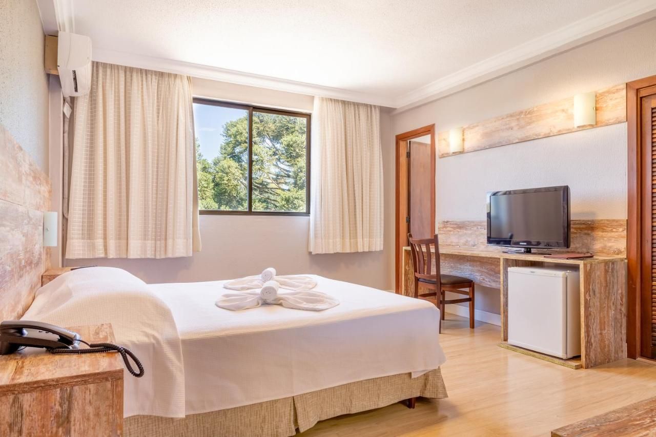 Um quarto de hotel com uma cama, televisão, escrivaninha e cadeira.