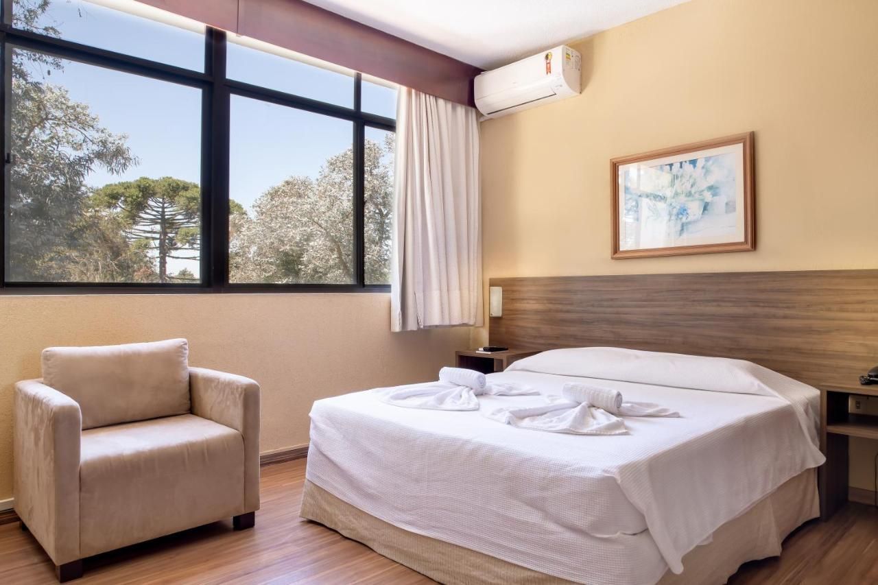 Um quarto de hotel com uma cama, cadeira e janela.