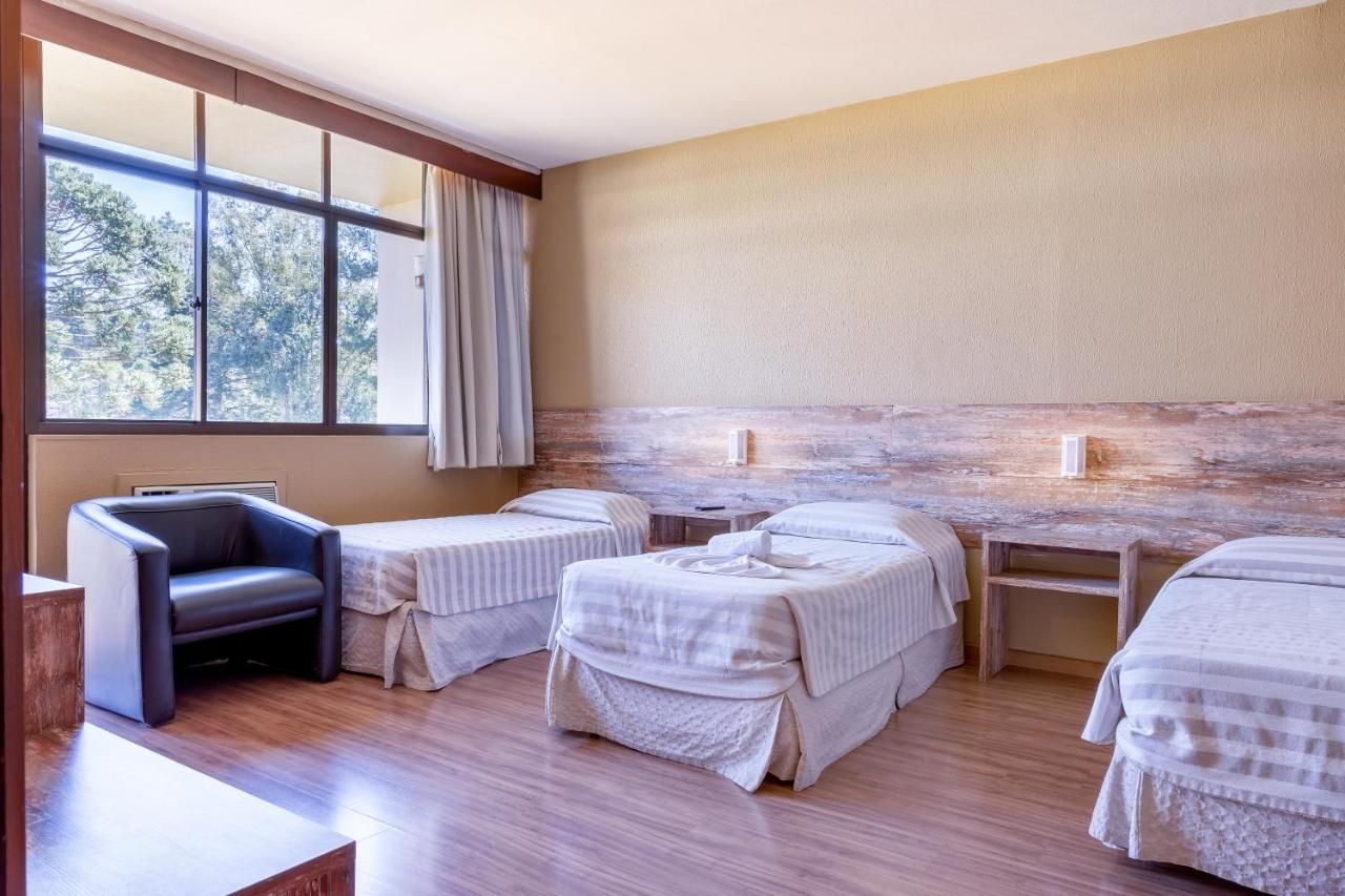 Um quarto de hotel com três camas, uma cadeira e uma janela.