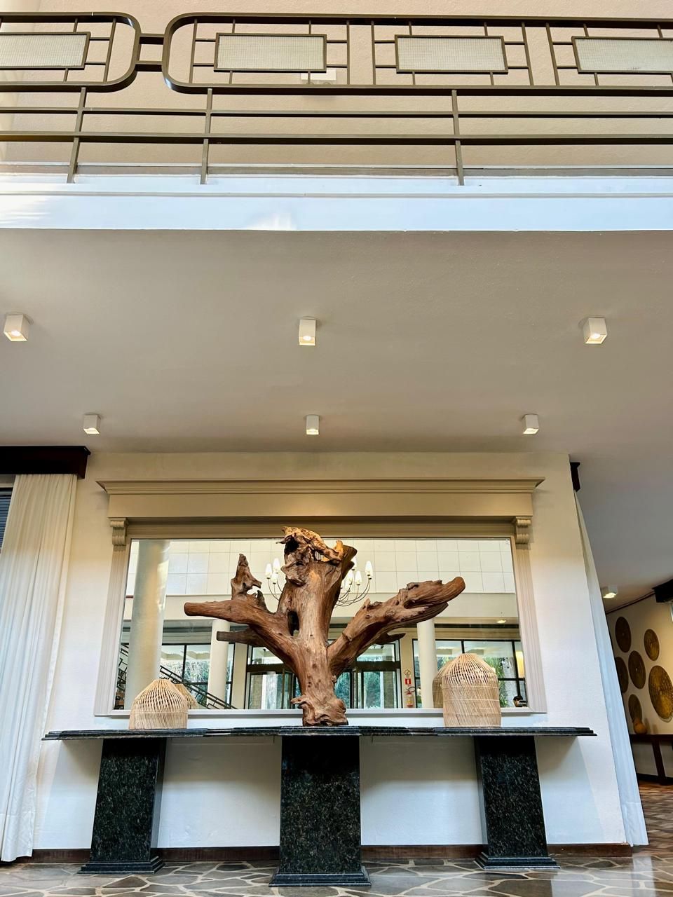 Uma grande escultura de madeira está sobre uma mesa em frente a uma janela.