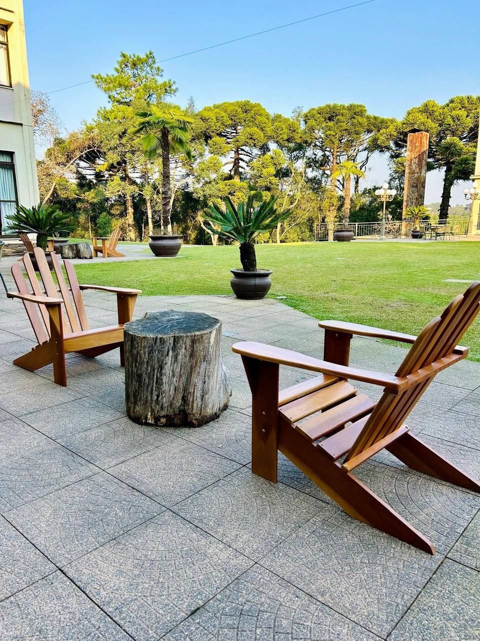 Duas cadeiras de madeira estão em um pátio ao lado de um toco de árvore.