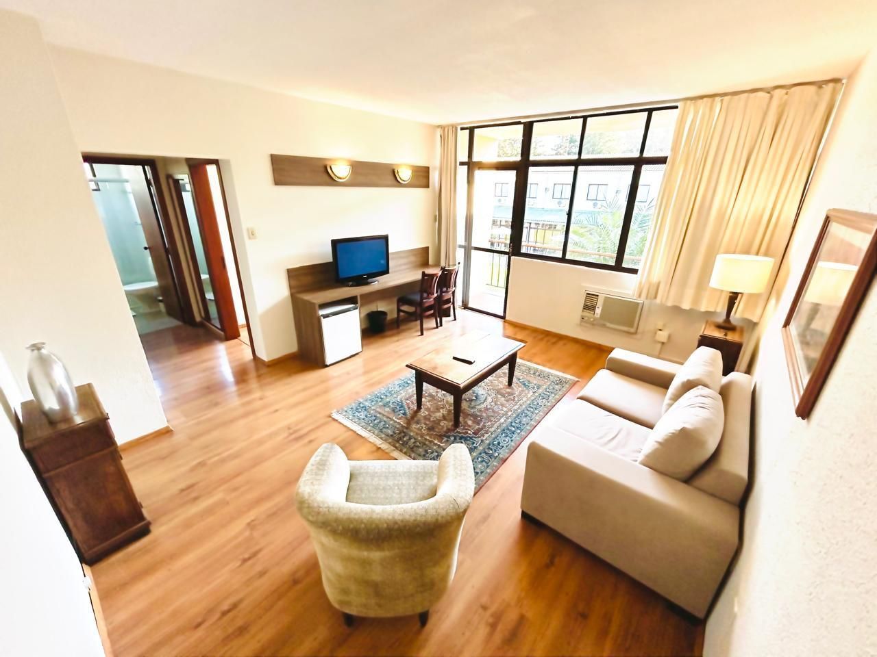 Uma sala de estar com sofá, cadeira, mesa e televisão.