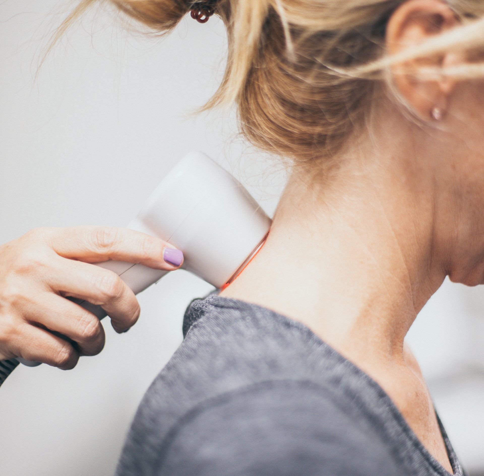 a woman with purple nail polish is using a device on her neck