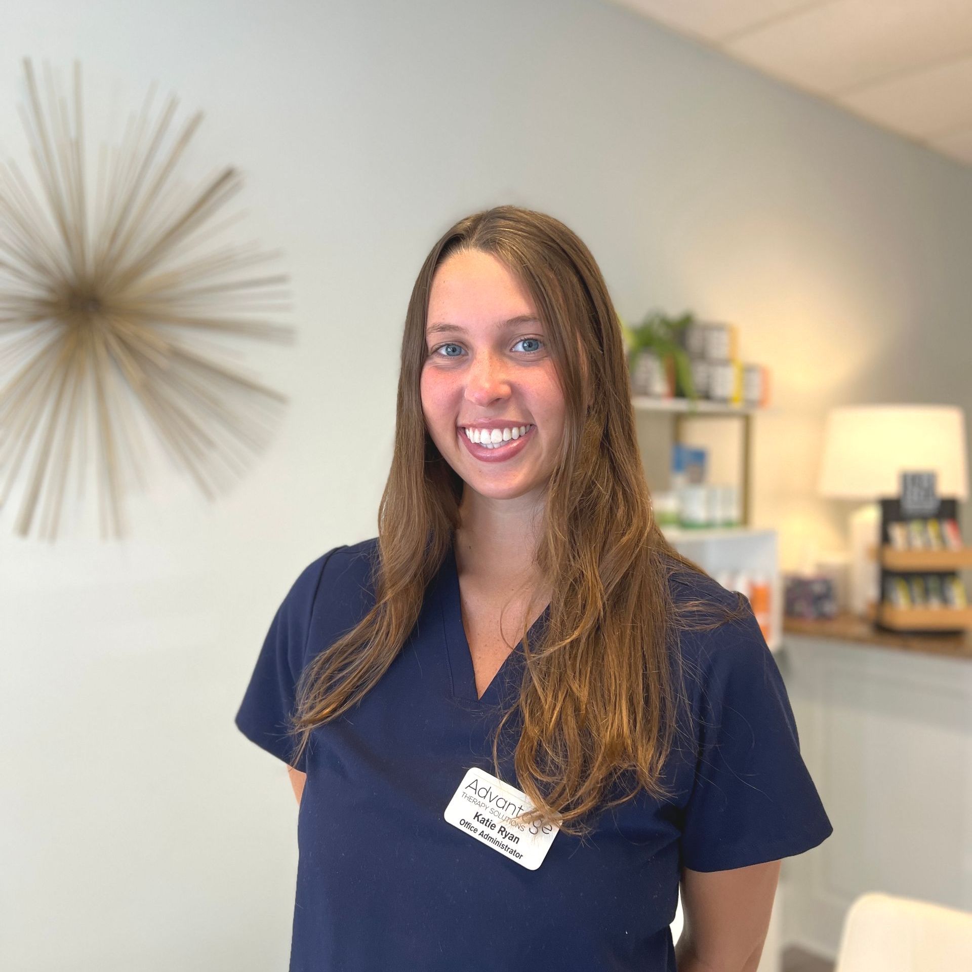 a woman in a blue scrub top is smiling in a waiting room .