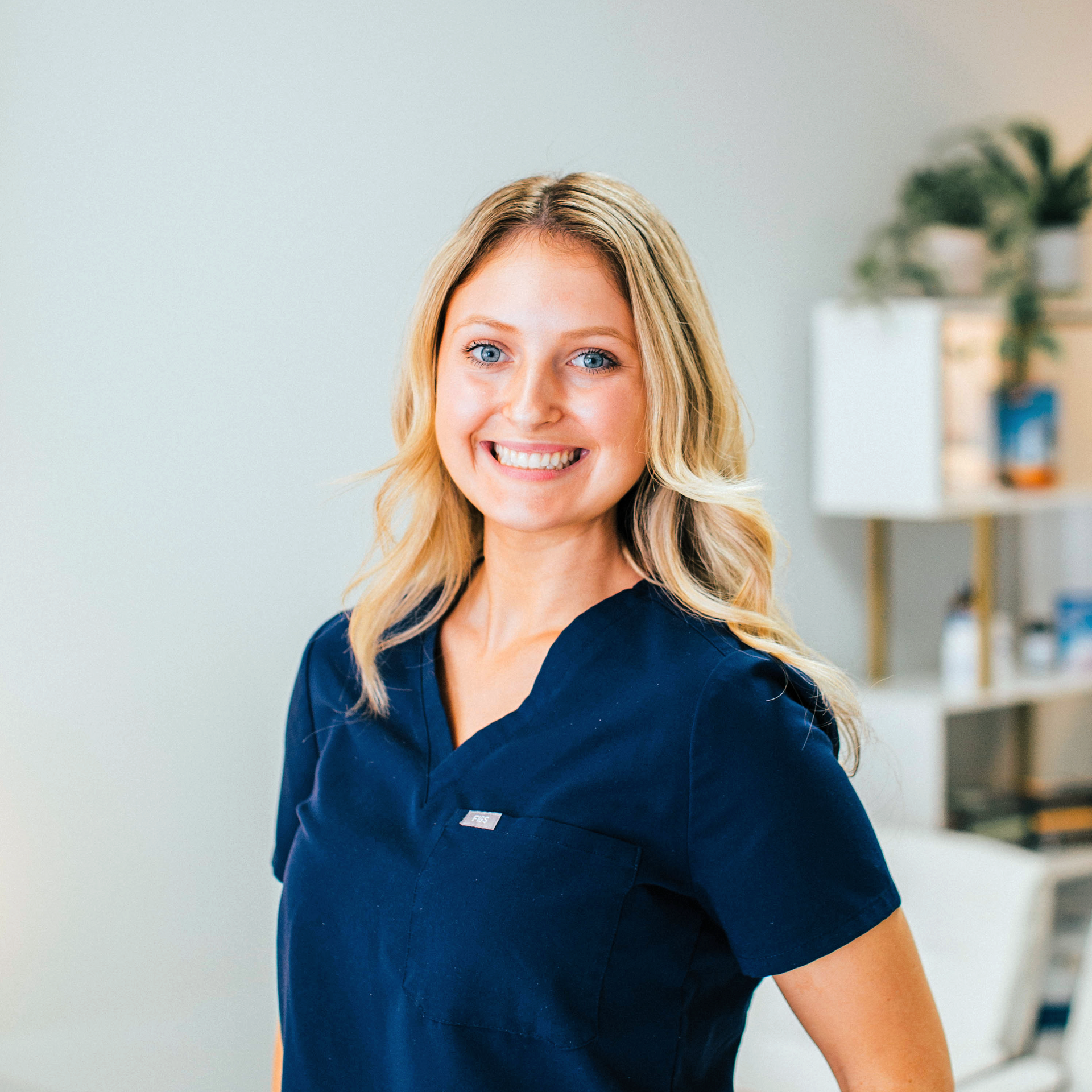 a woman in a blue scrub top is smiling in a waiting room .