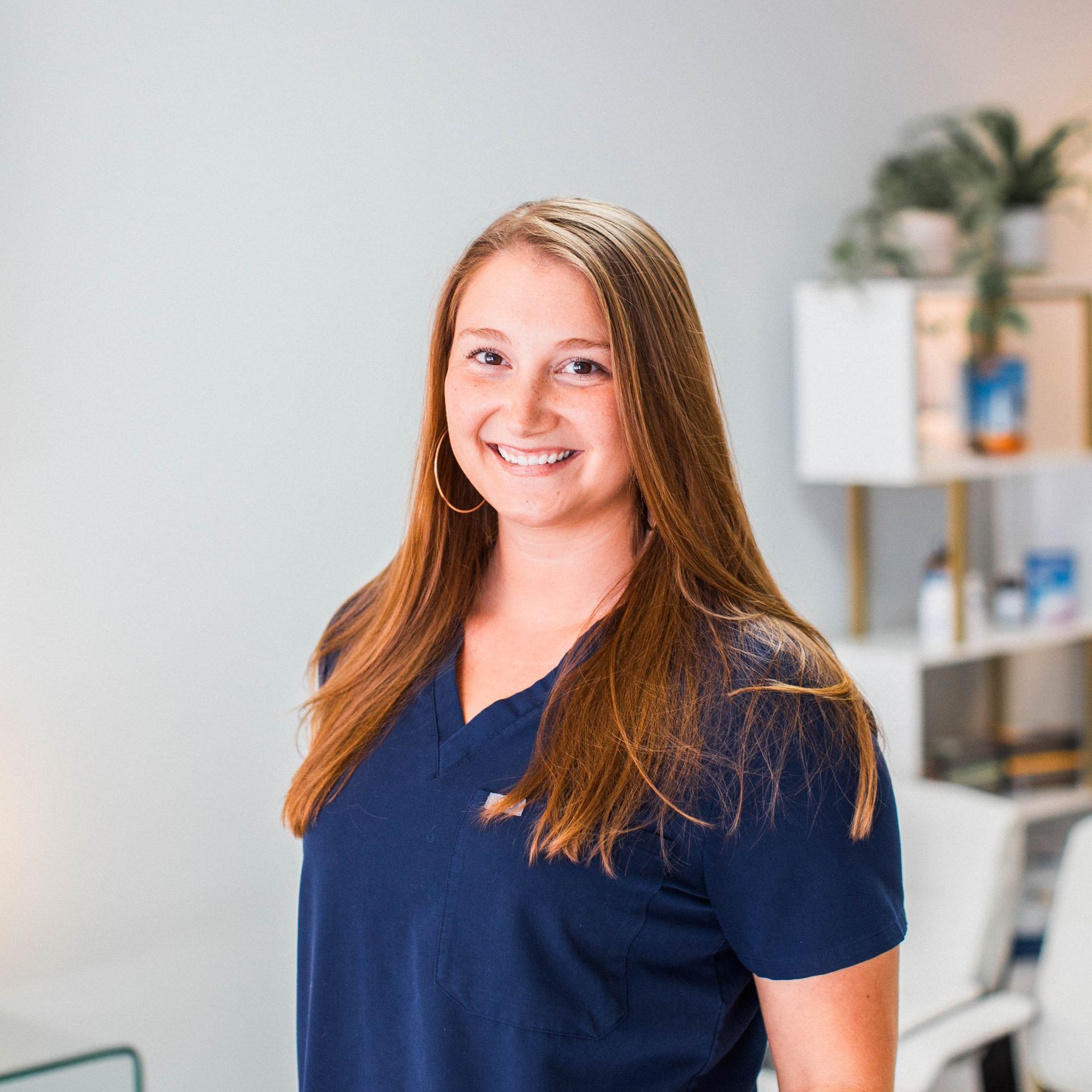 a woman in a blue scrub top is smiling in a living room