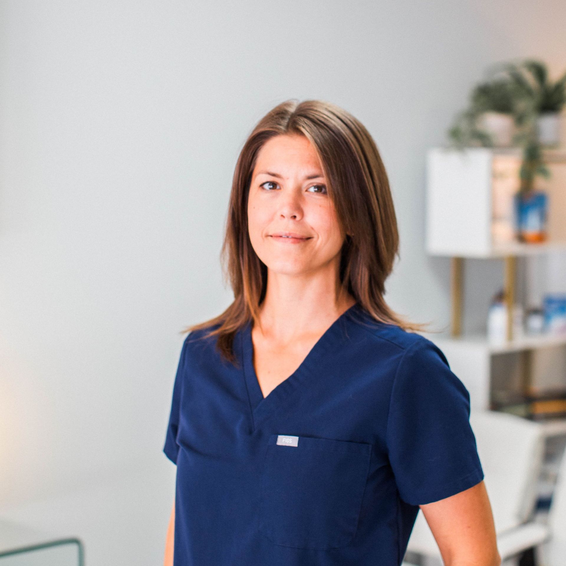 a woman in a blue scrub top is standing in a waiting room .