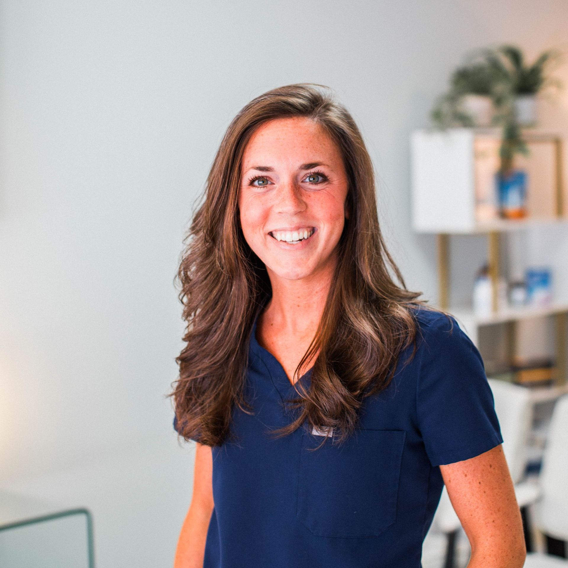 a woman in a blue scrub top is smiling for the camera