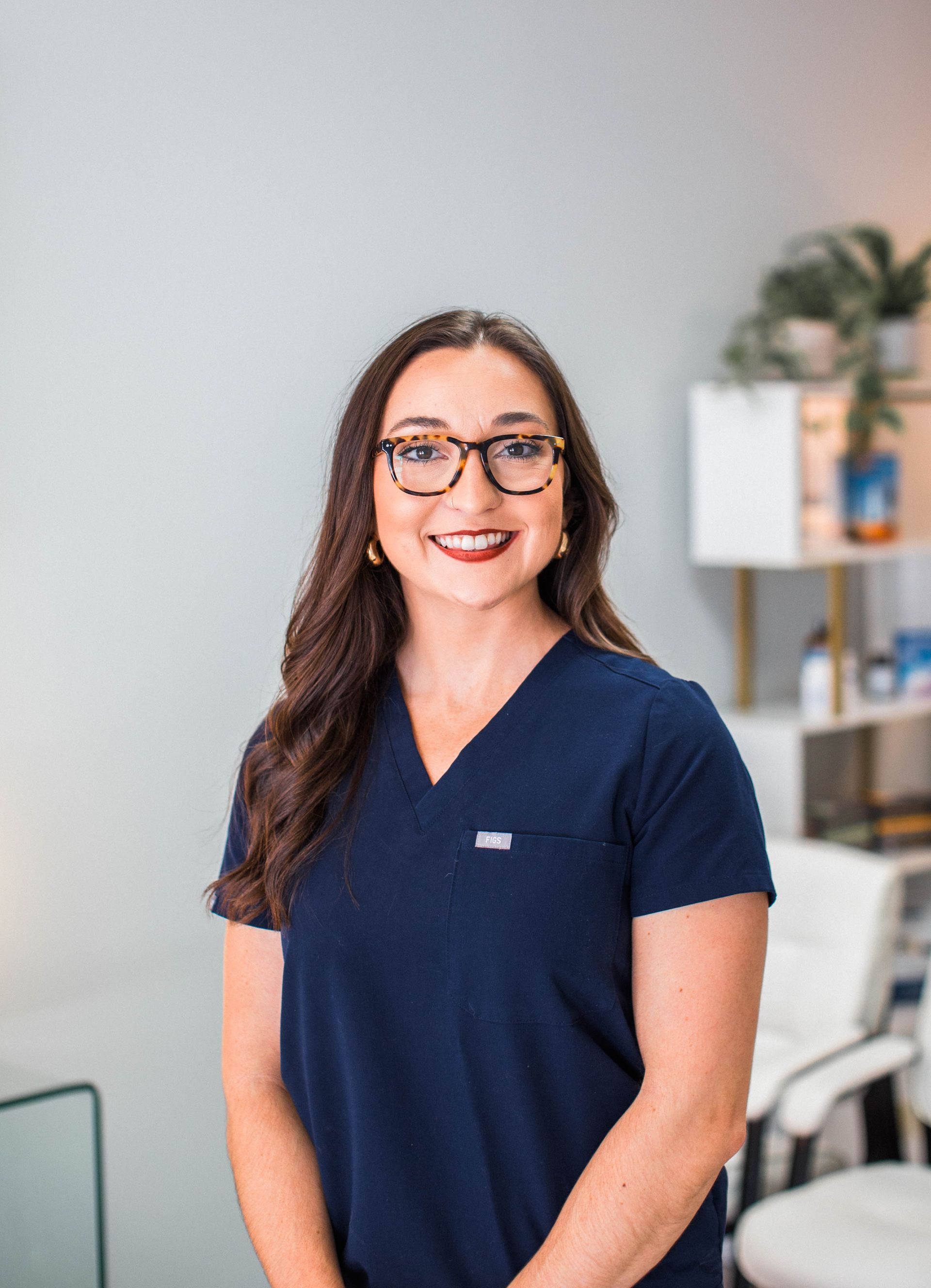 a woman wearing glasses and a blue scrub top smiles for the camera