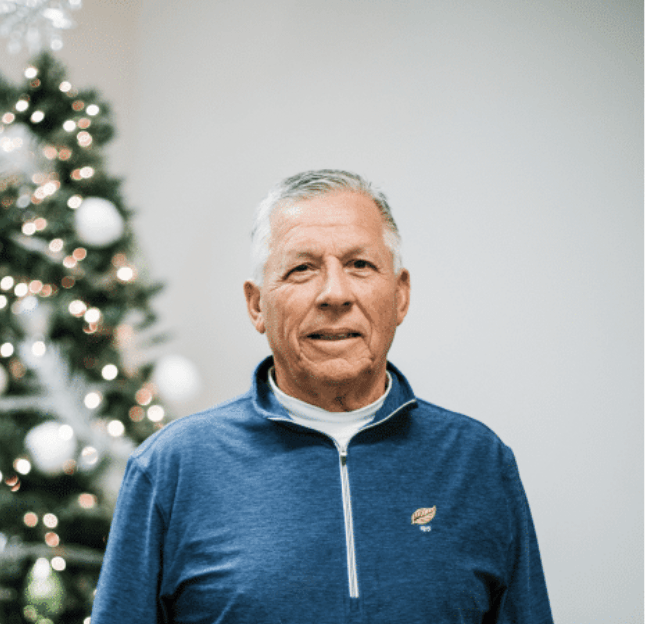 A man in a blue shirt is standing in front of a christmas tree.