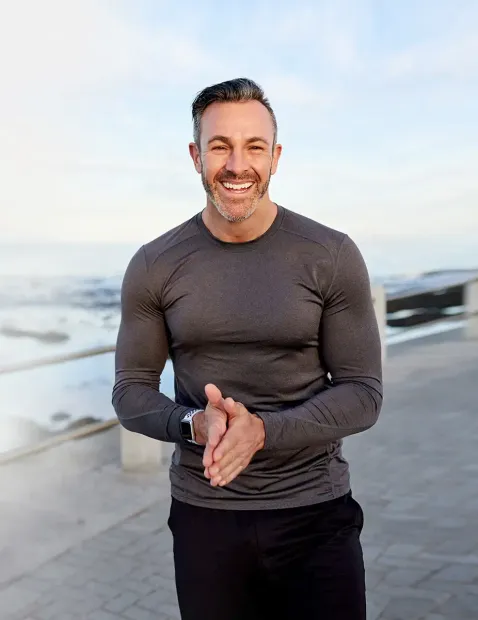 A man with a beard is wearing a gray shirt and smiling.